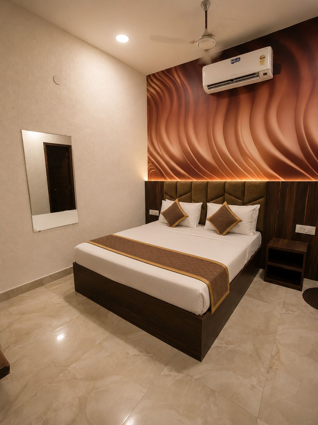 A modern hotel room with a large bed, a wall-mounted air conditioner, and a ceiling fan.