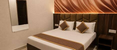 A modern hotel room with a large bed, a wall-mounted air conditioner, and a ceiling fan.