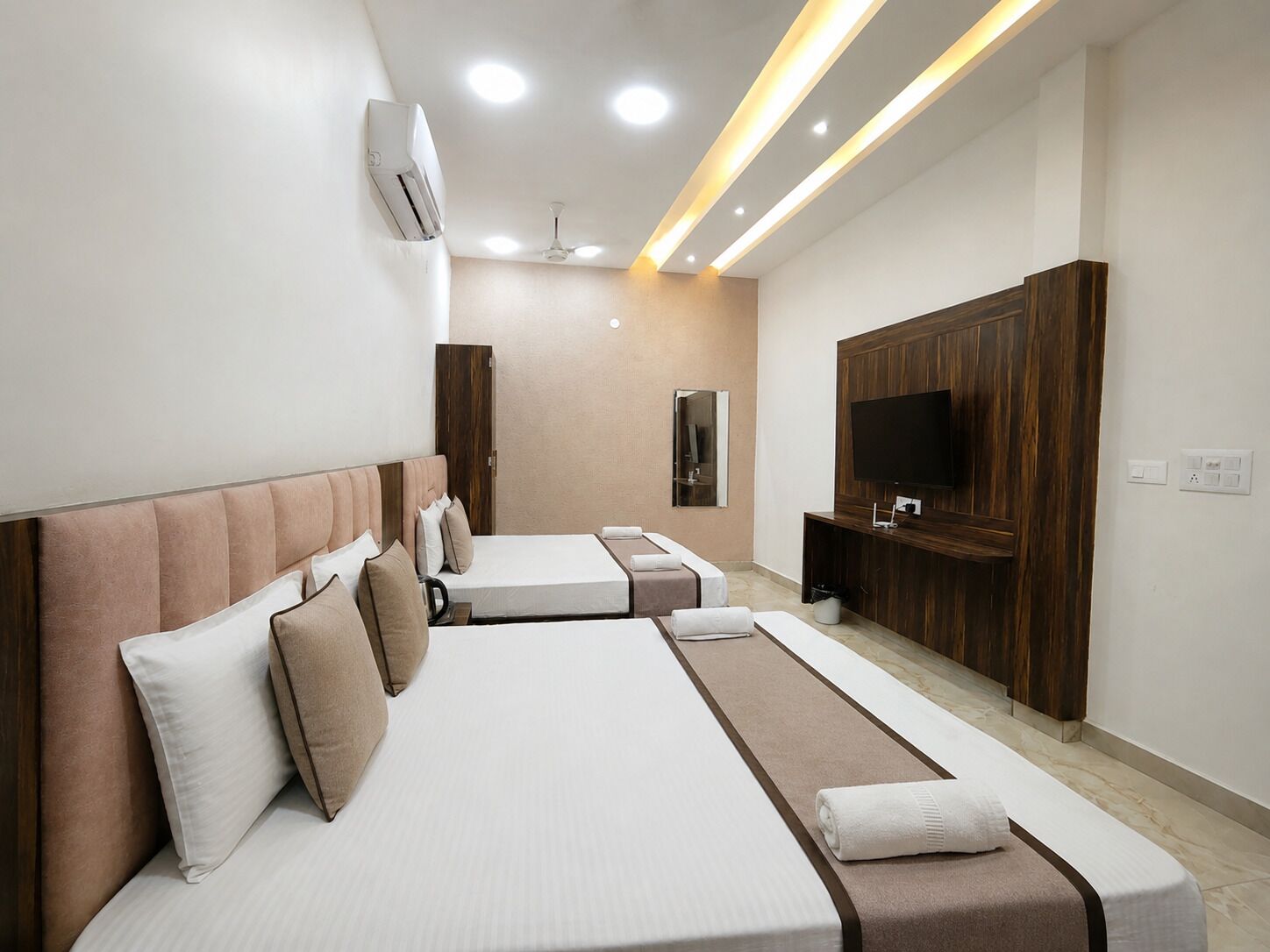 A hotel room with two beds, a TV, a ceiling fan, and recessed lighting.