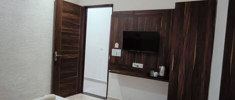 A hotel room with a bed, a TV mounted on a wooden panel, a door, and a small blue bucket.