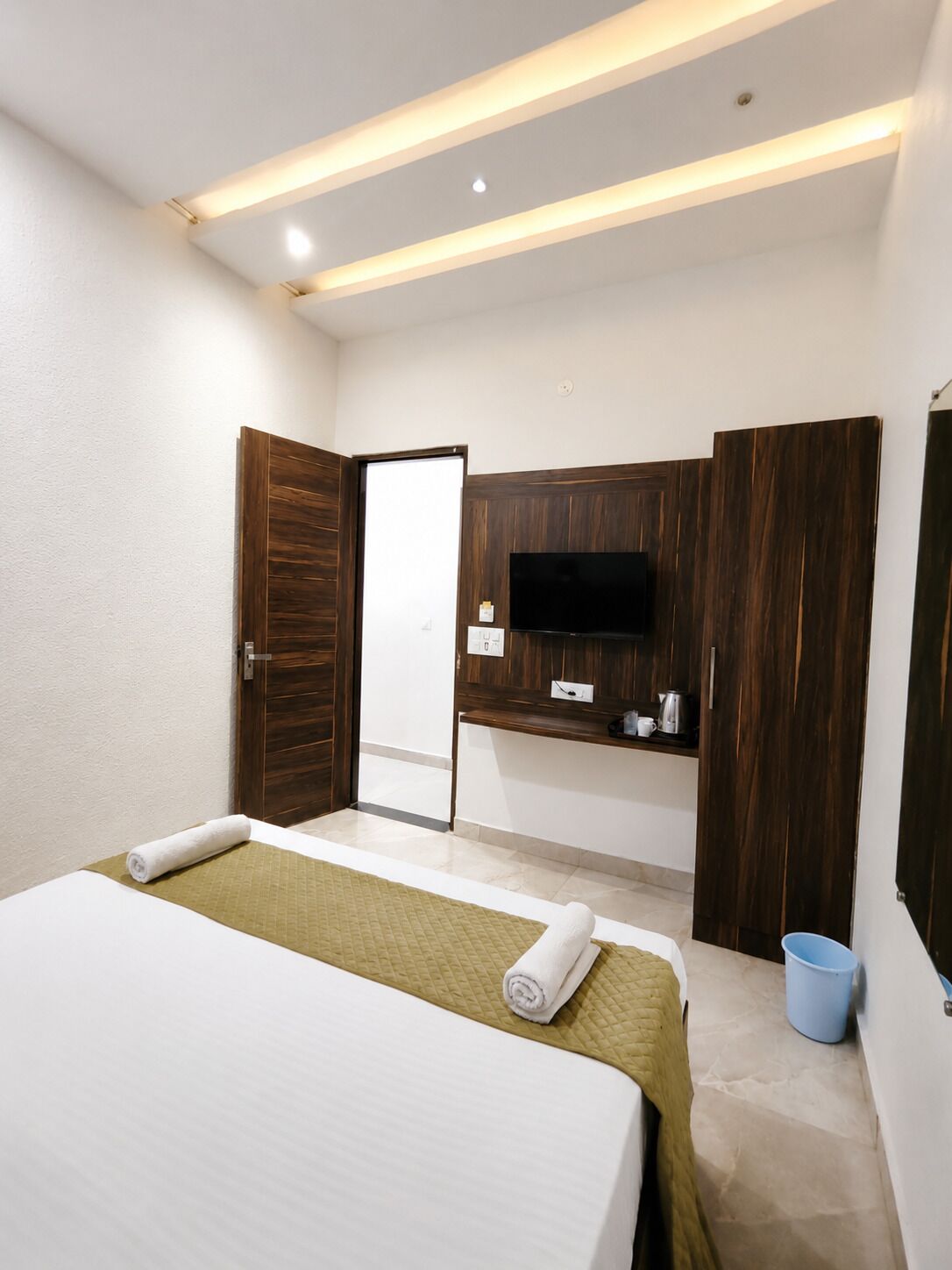 A hotel room with a bed, a TV, a wooden wardrobe, and a small kitchenette.
