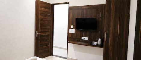 A hotel room with a bed, a TV, a wooden wardrobe, and a small kitchenette.