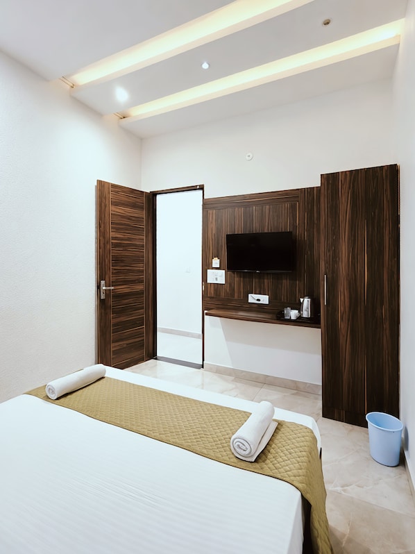 Une chambre dâhĂŽtel avec un lit, un tĂ©lĂ©viseur fixĂ© sur un panneau en bois, une porte et une petite table sur laquelle se trouvent une bouilloire et des tasses.