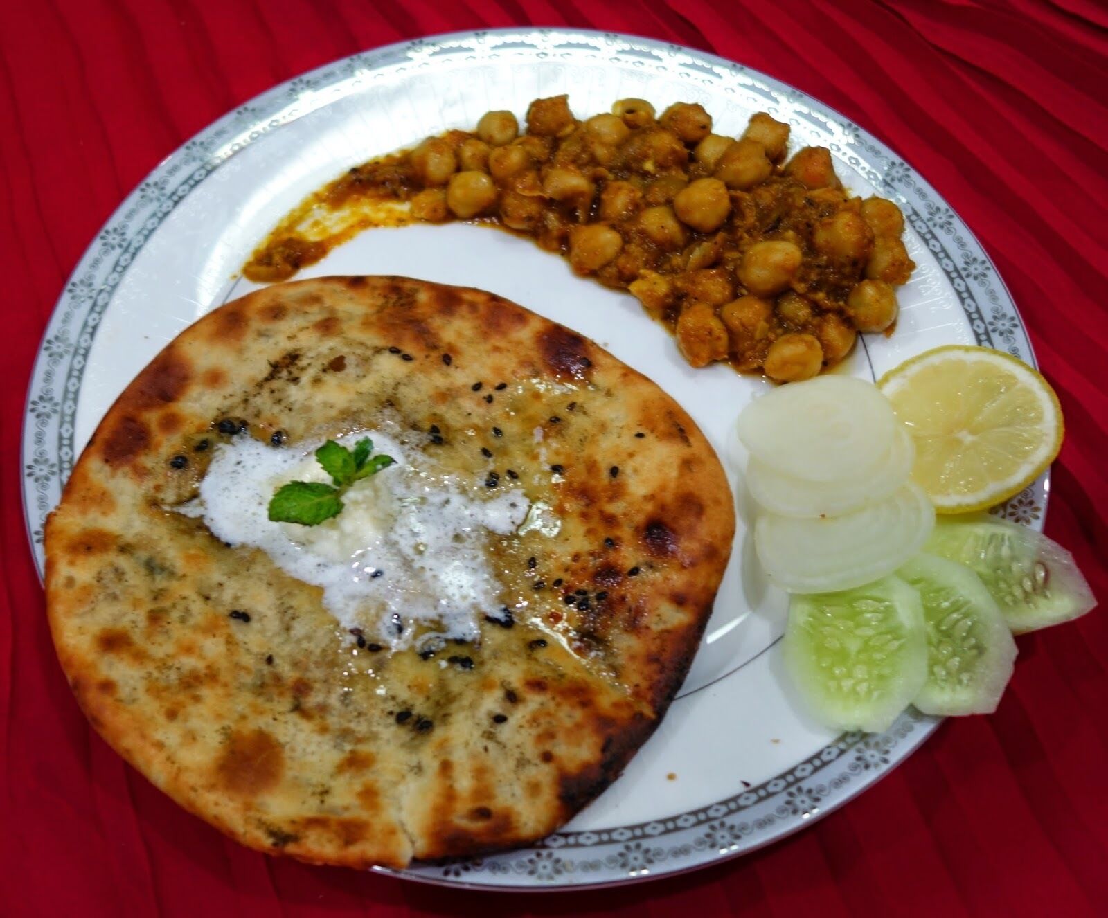 A plate with a flatbread topped with yogurt and herbs, chickpeas, and sliced cucumbers.