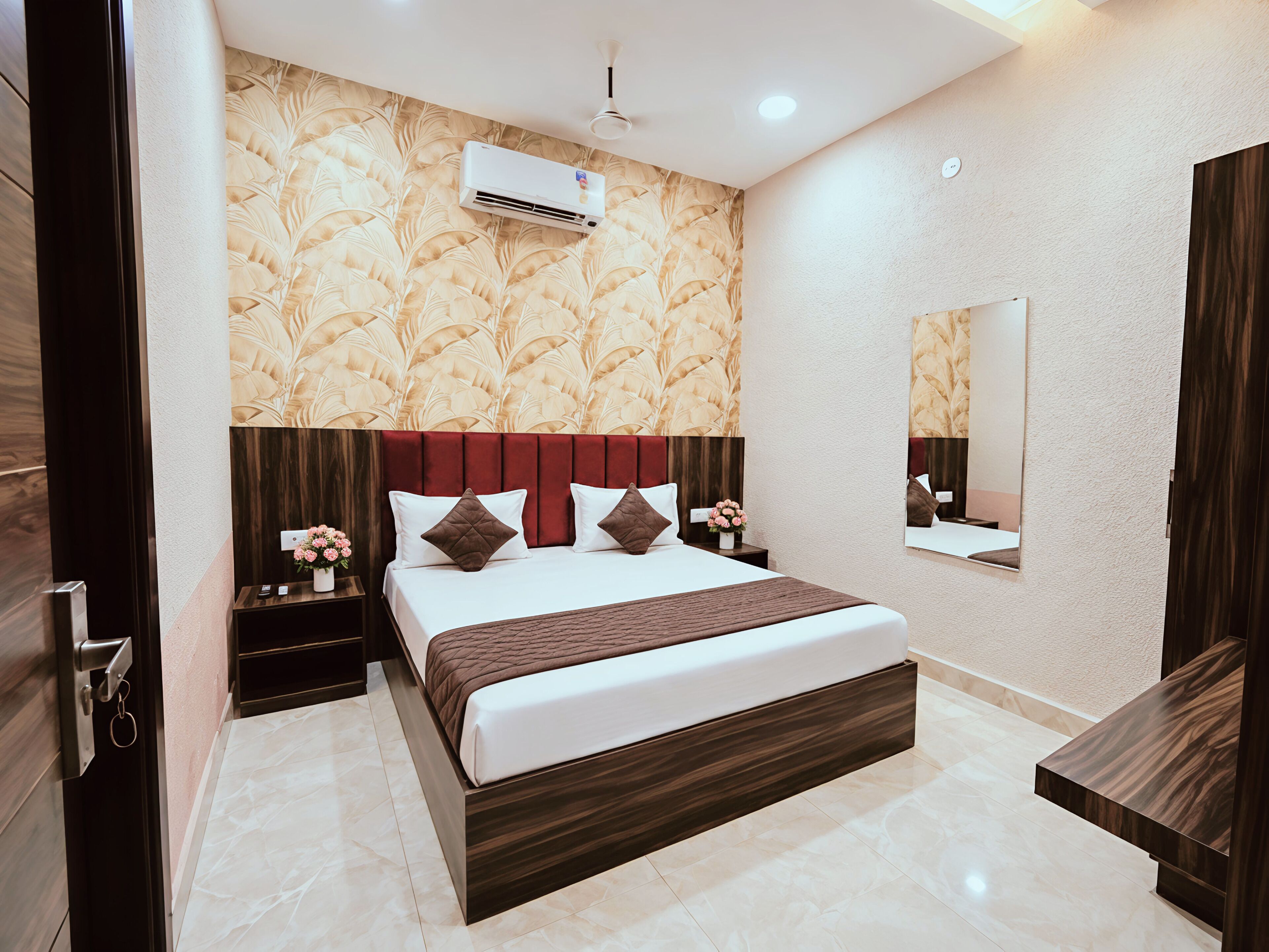A modern hotel room with a large bed, a nightstand, an air conditioning unit, a mirror, and a wooden wardrobe.