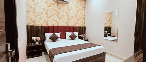 A modern hotel room with a large bed, a nightstand, an air conditioning unit, a mirror, and a wooden wardrobe.