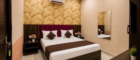 A hotel room with a bed, a nightstand, a mirror, and a wall-mounted air conditioner.