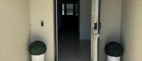 Una puerta que da a un pasillo con un felpudo que dice 'homes' y dos macetas a cada lado.