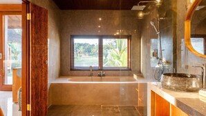A modern bathroom with a freestanding bathtub, a large mirror, and a window with a view of greenery. - Bagus Bandem Villa (Sebatu)