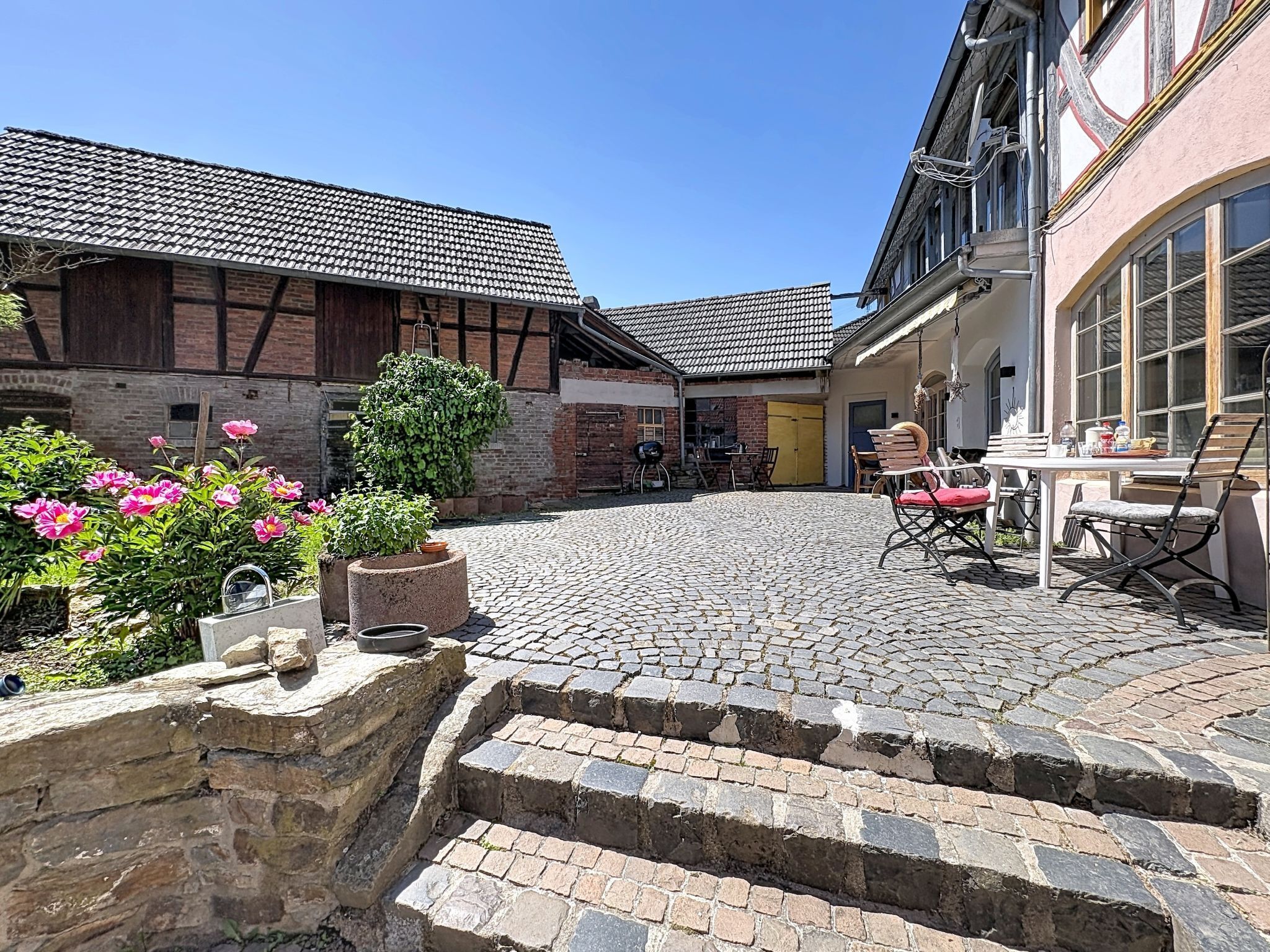 Ein Innenhof mit Kopfsteinpflaster, einer Steinsäule und einem Tisch mit Stühlen.