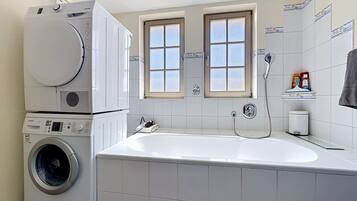 Ein kleines Badezimmer mit Waschmaschine, Badewanne und Fenster.