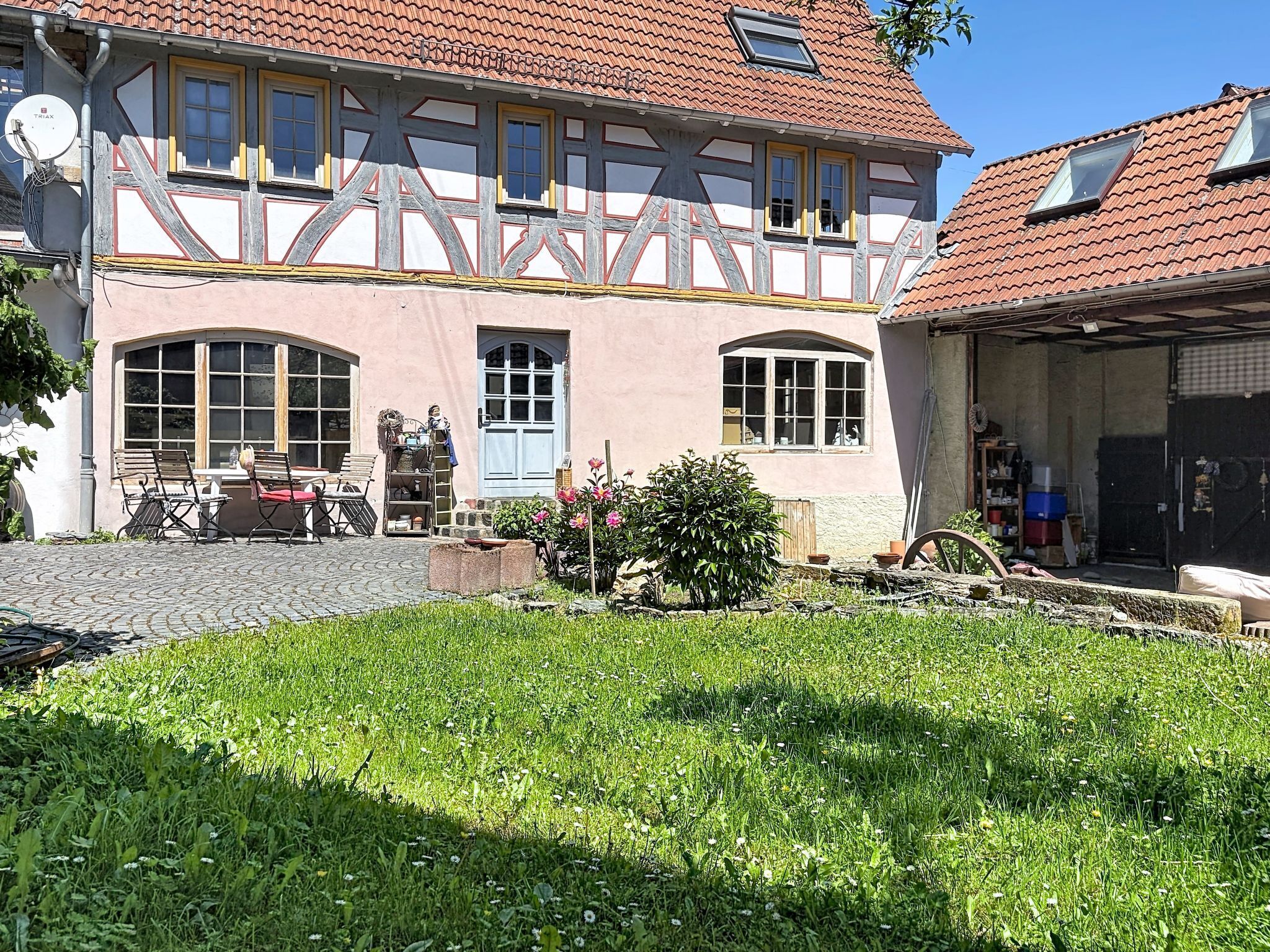 Ein traditionelles Fachwerkhäuschen mit Garten, Sitzgelegenheit im Freien und einer sichtbaren Satellitenschüssel.