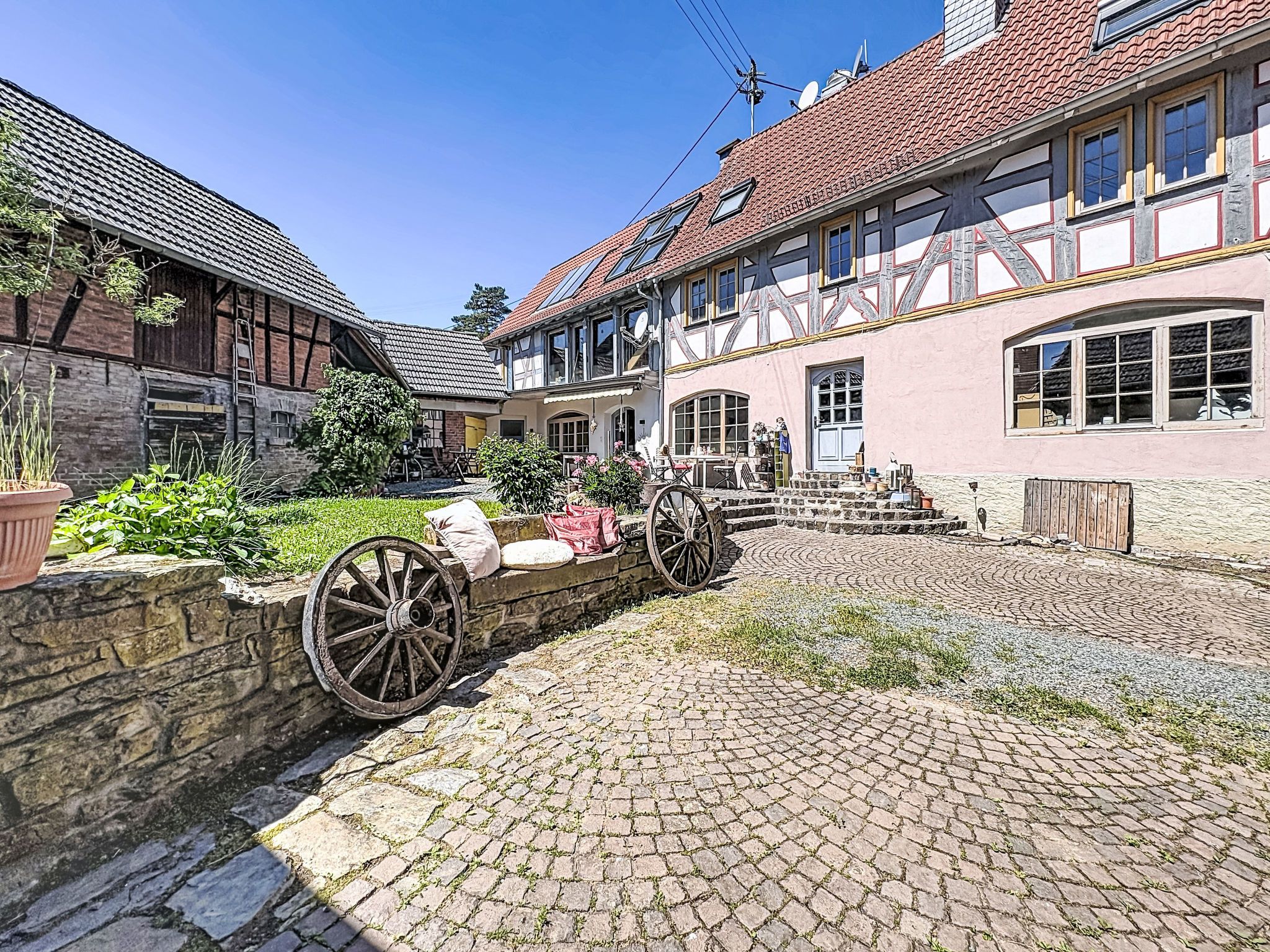 A traditional European courtyard with cobblestone paving, a wooden cart, and a stone wall.