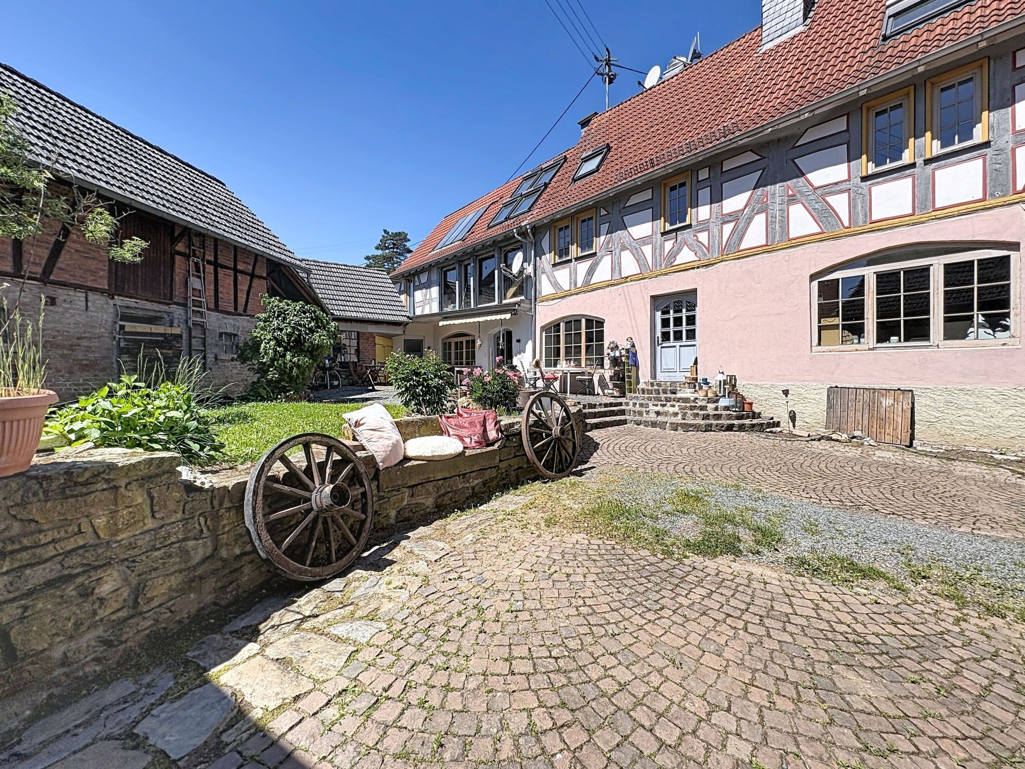 A traditional half-timbered house with a cobblestone courtyard, a stone wall, and a wooden cart.