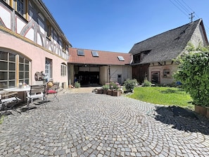 A courtyard with cobblestone paving, a building with a red-tiled roof, and a garden area with potted plants. - Alte Scheune by Interhome (Idstein)