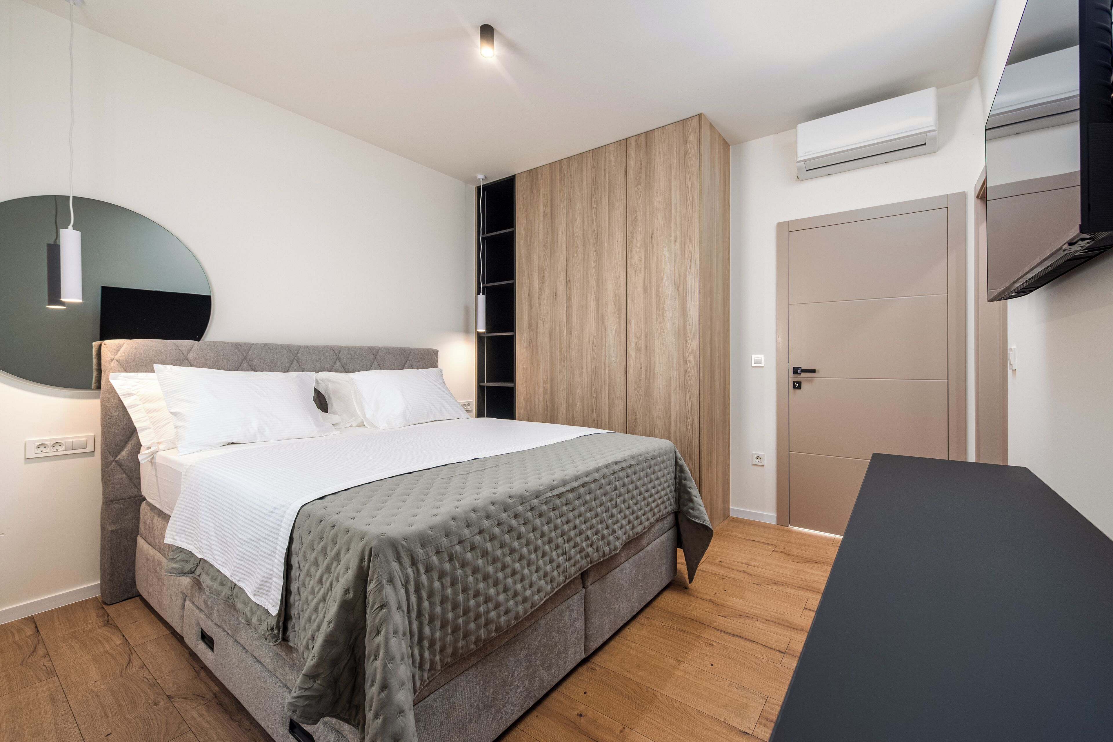 A modern bedroom with a bed, bedside table, wardrobe, and built-in TV.