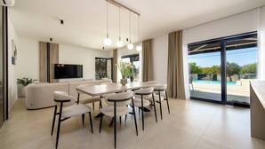 Una sala de estar moderna con sofá, mesa de comedor, sillas, televisor y un amplio ventanal con vistas.
