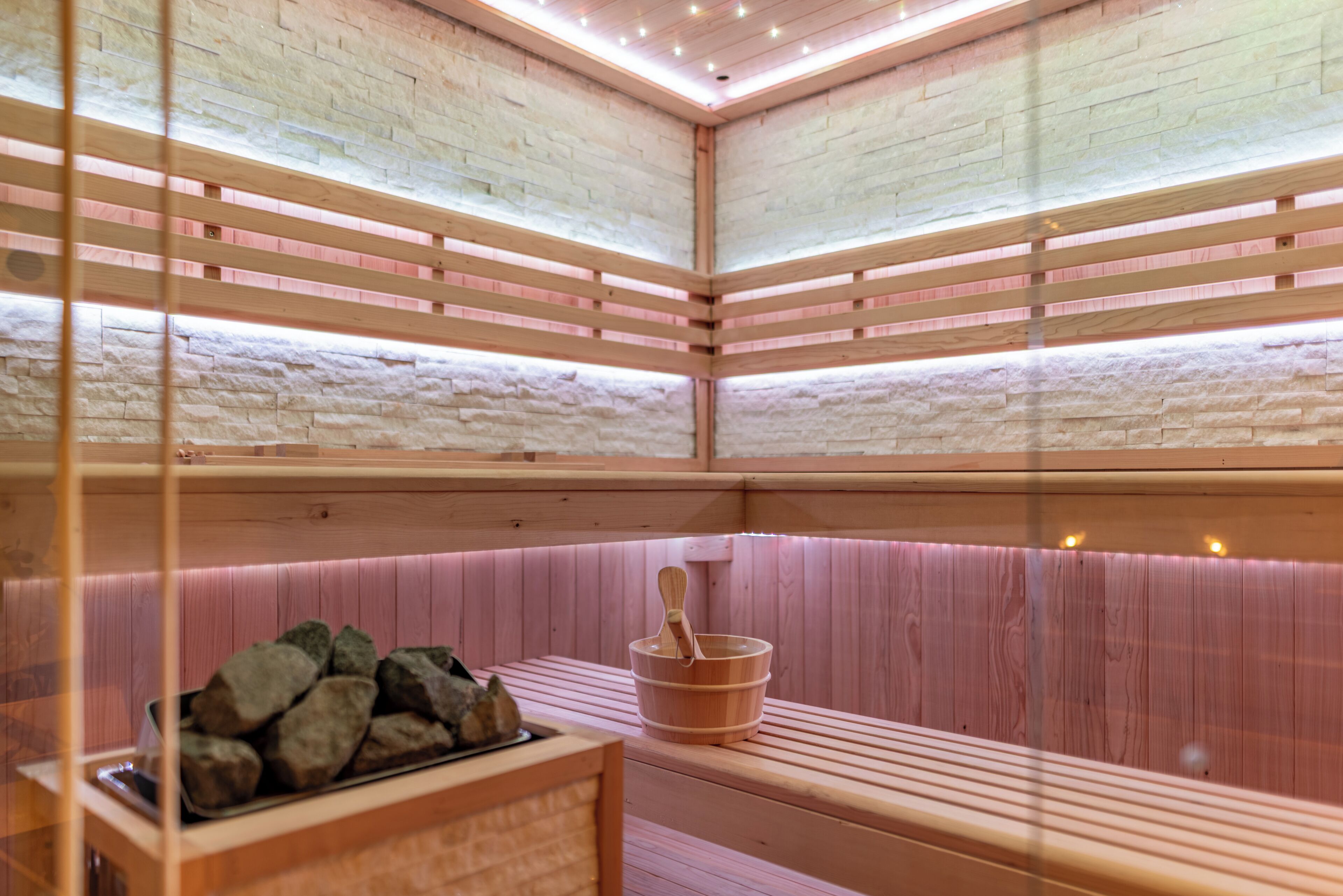 A sauna with wooden benches, a wooden bucket, and a rock-filled container.