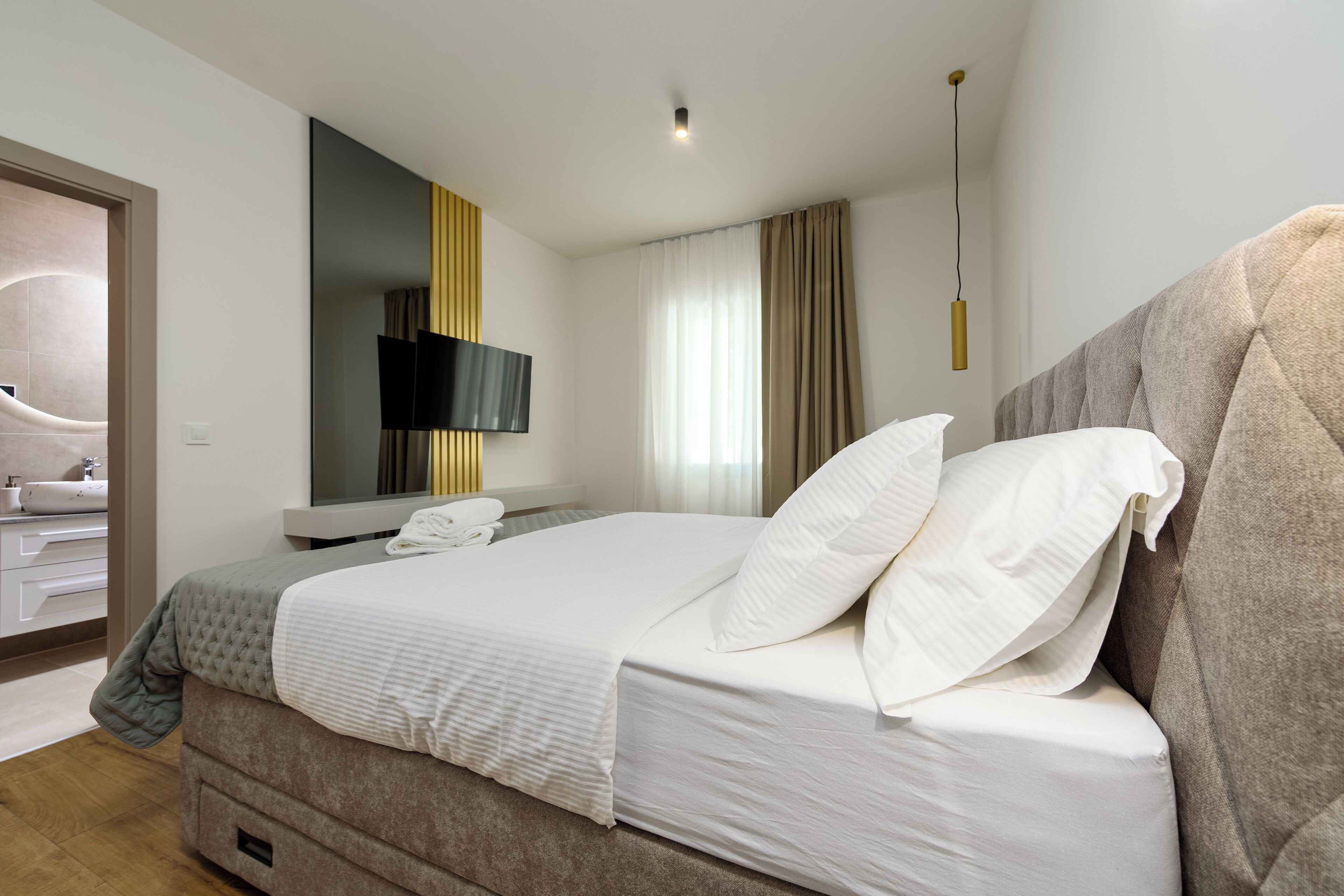 Una habitación de hotel con cama, televisión, baño y ventana con cortinas.