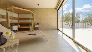 Una habitación moderna con un ventanal grande, una cama, un banco de madera y una mesa de vidrio con una botella y un vaso.