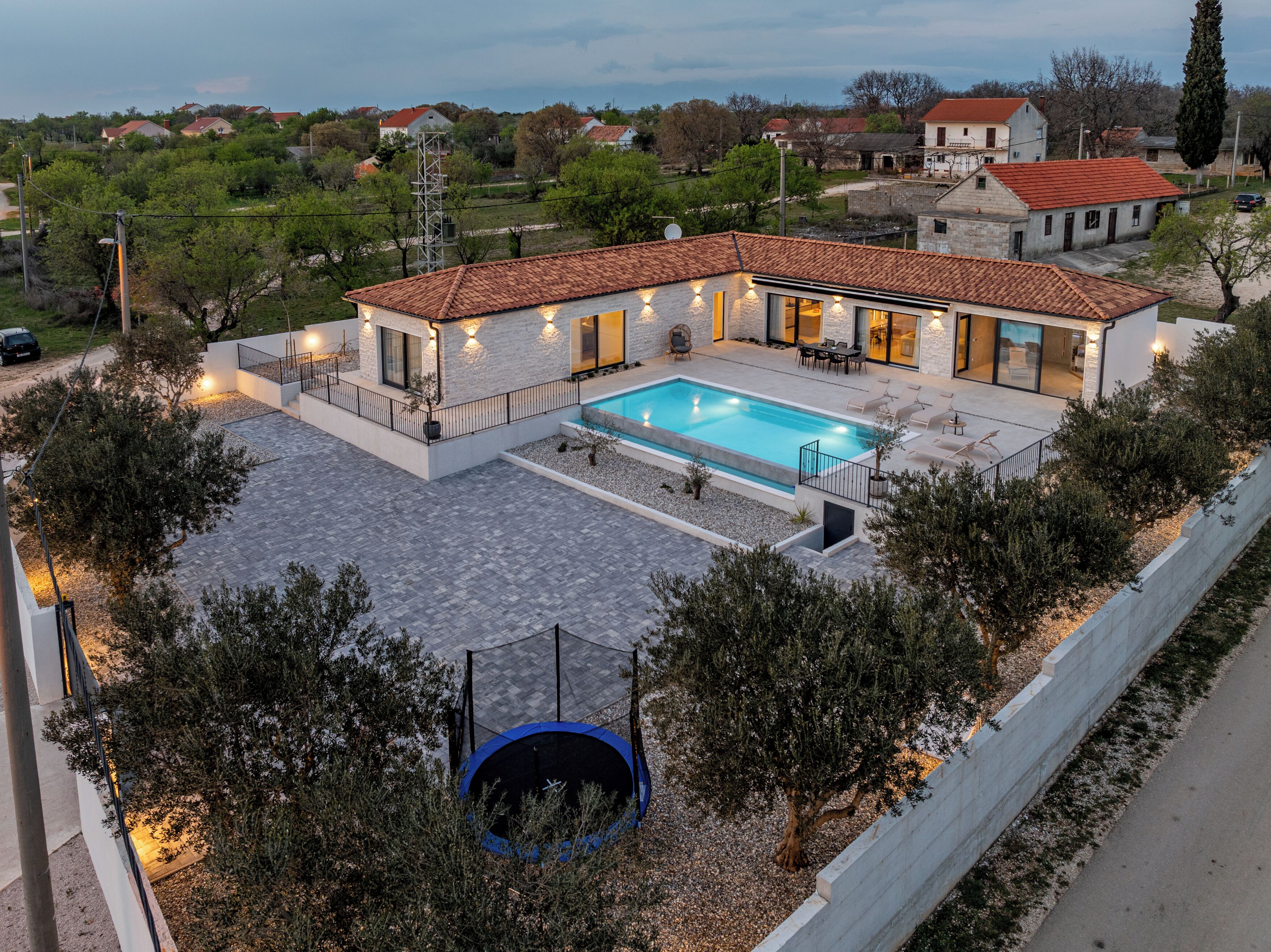 A modern house with a swimming pool, outdoor seating, and a trampoline.