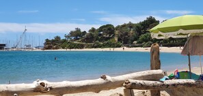 A beach with boats, a green umbrella, and a wooden fence. - Apartment T3 3*, 200m from the beach, 57m², 2 bedrooms, air conditioning, parking, terrace, balcony, shops (Bormes-les-Mimosas)