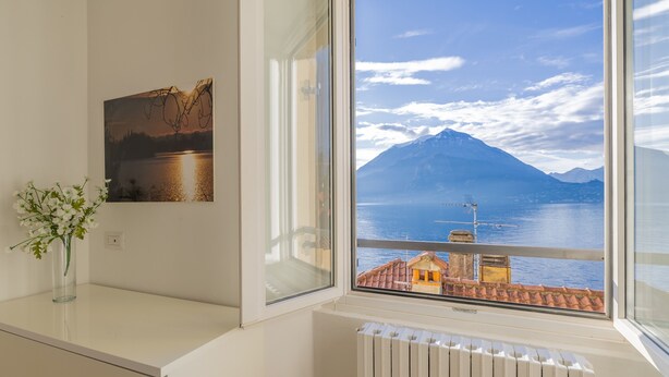A room with a window view of a mountain and lake, a radiator, a vase with flowers, and a picture on the wall. - Stunning View in Varenna (Varenna)