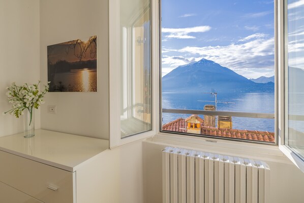 Ein Zimmer mit Blick auf einen Berg und einen See, ein Heizkörper, eine Vase mit Blumen und ein Bild an der Wand.
