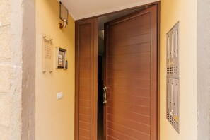 Ein Hotel Eingang mit einer Holztür, einer Wandleuchte und einem Verteilerkasten.