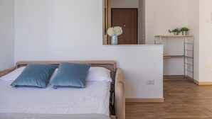 A bedroom with a bed, pillows, a nightstand, a mirror, a small shelf with plants, and a wooden floor. - Stunning View in Varenna (Varenna)