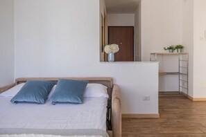 Ein Schlafzimmer mit einem Bett, Kissen, einem Nachttisch, einem Spiegel, einer kleinen Ablage mit Pflanzen und Holzdielen.