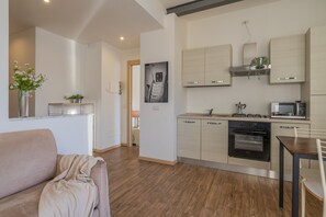 Eine moderne Küche mit integrierten Geräten, ein Essbereich mit Tisch und Stühlen sowie ein Wohnzimmer mit einer Couch.