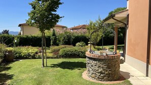 Ein Garten mit einem Steinfountain, einem Baum und einem Gebäude mit einem Ziegeldach.