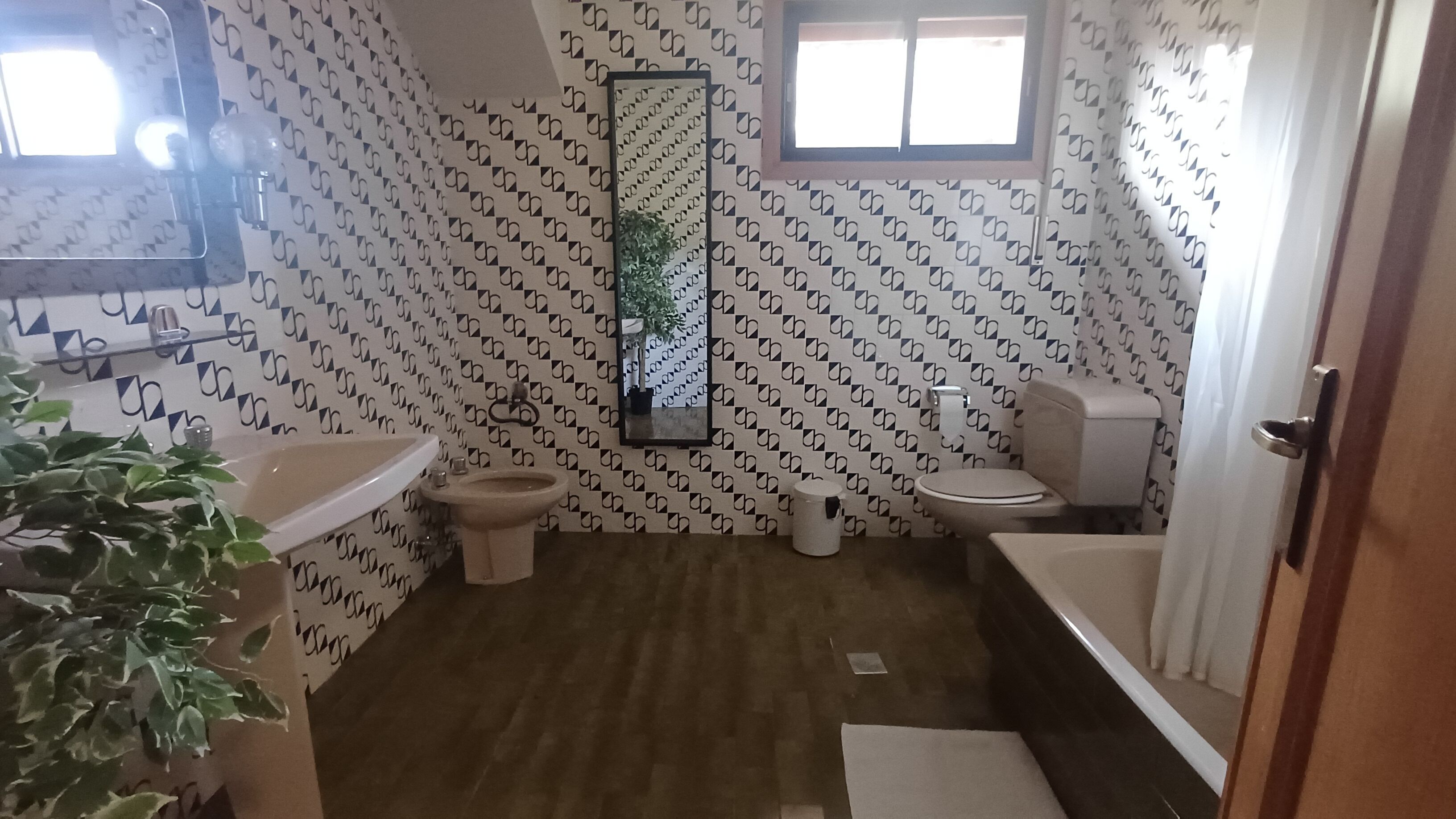 A bathroom with a patterned wall, a toilet, a bidet, a sink, and a mirror.