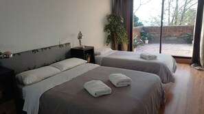 Ein Hotelzimmer mit zwei Betten, einem Nachttisch, einer Lampe, einem Blumentopf und Blick ins Freie.