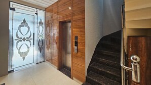 A modern interior with a wooden wall, a glass door with a decorative pattern, and a staircase with metal railings. - Hotel CSJS International (Amritsar)