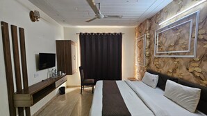 A bedroom with a bed, a TV, a wardrobe, a chair, and a ceiling fan. - Hotel CSJS International (Amritsar)
