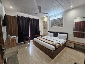 A modern bedroom with a large bed, a desk, a chair, a ceiling fan, and artwork on the walls.