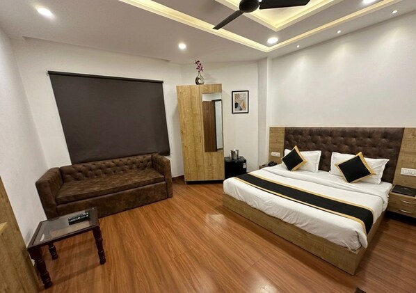 A bedroom with a bed, a sofa, a small table, a mirror, and a ceiling fan.
