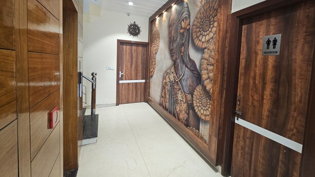 A hallway with wooden paneling, a mural, a door with a 'WASHROOM' sign, and a security camera. - Hotel CSJS International (Amritsar)
