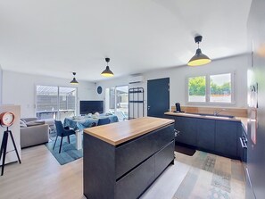 Een moderne keuken met een centraal eiland, een eetgedeelte met tafel en stoelen, en een woonkamer met een bank en televisie.