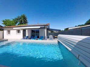 A swimming pool with lounge chairs, a covered seating area, and a building with windows and a tiled roof. - Le Bayonnais by Interhome (Bénesse-Maremne)