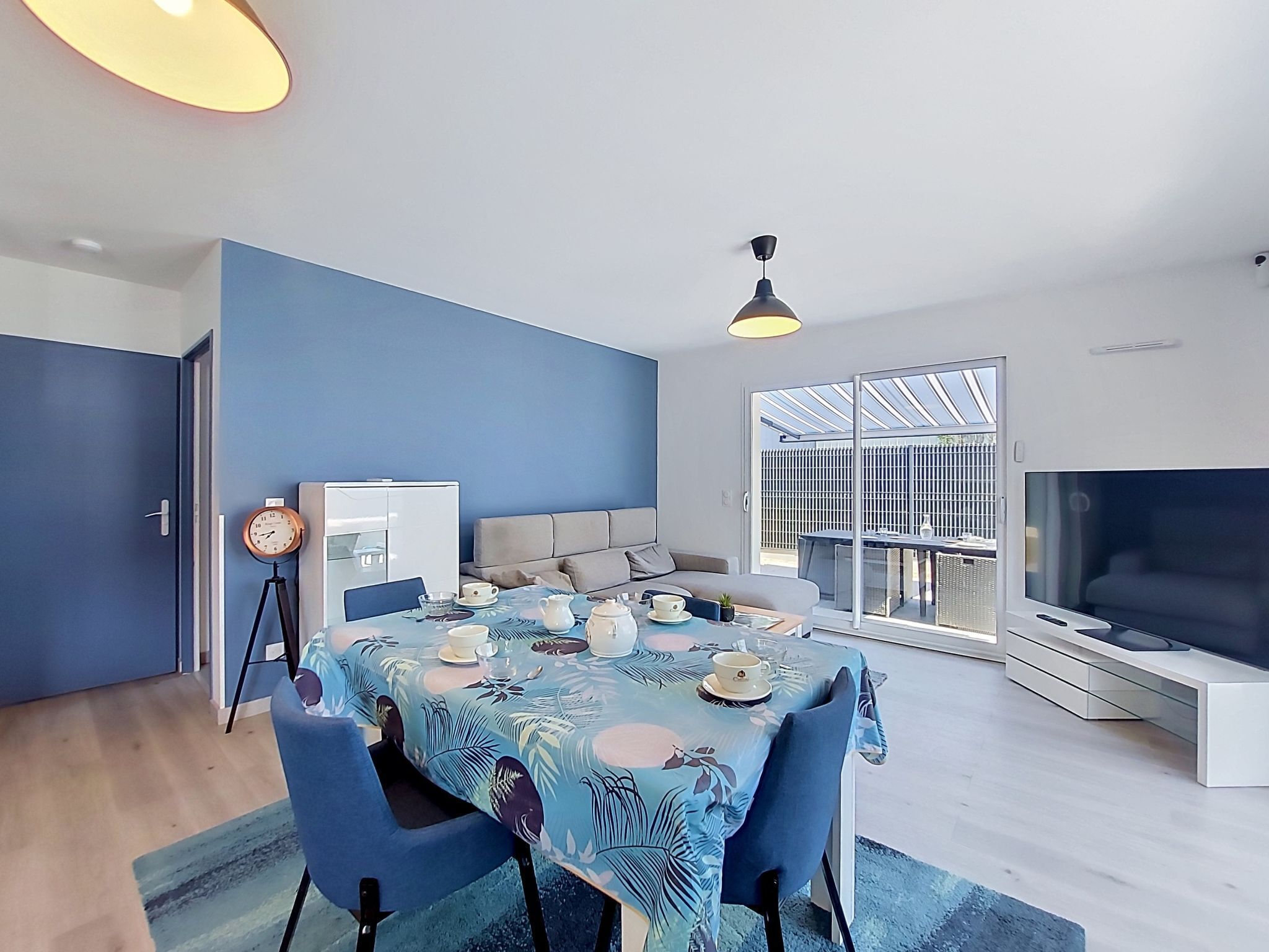 A modern living room with a dining area, a large TV, and a balcony with a view.