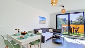 Ein modernes Wohnzimmer mit Esstisch, grünen Stühlen, einer Couch und einem Balkon mit Gartenmöbeln.