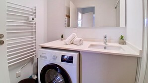 Ein modernes Badezimmer mit einer Siemens Waschmaschine, einem Waschbecken, einem Spiegel und einem Handtuchhalter.