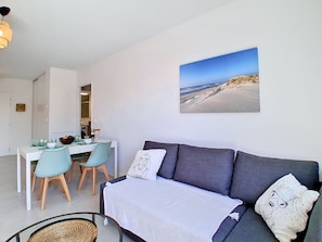 A modern living room with a grey sofa, a dining table with chairs, and a beach scene painting on the wall. - Résidences du Lac by Interhome (Maubuisson)
