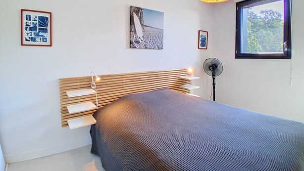 Ein modernes Schlafzimmer mit einem Bett, einem Standventilator, einem Fenster und Wandbildern.