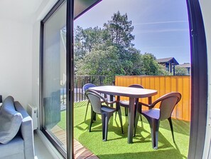 Ein Balkon mit Tisch und Stühlen, eine Glastür und Blick auf Bäume und einen Zaun.