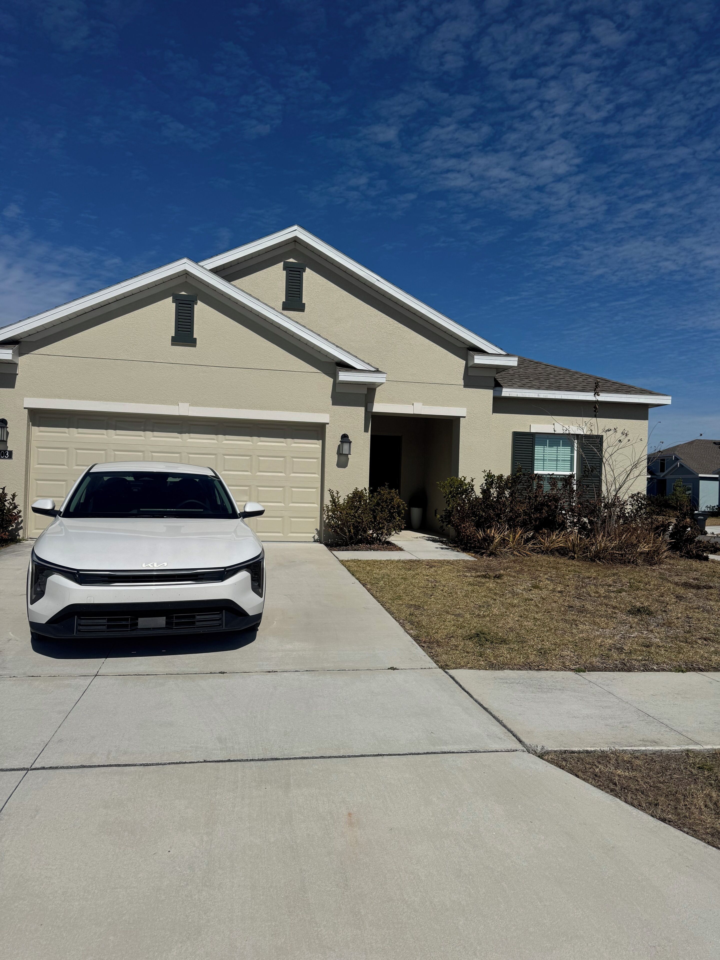 A residential house with a garage, a driveway, and a white car parked in front.