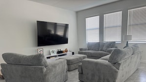 A modern living room with a large flat-screen TV, grey sofas, and a white entertainment unit. - Spacious 4-bedroom house in amazing Davenport with AC (Davenport)